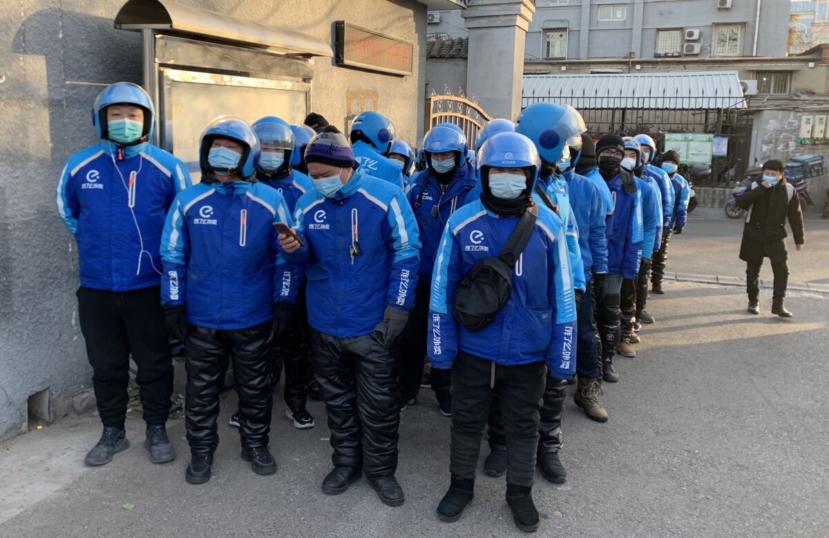 Men, wearing masks and matching clothing and helmets, stand in line outside a city building.