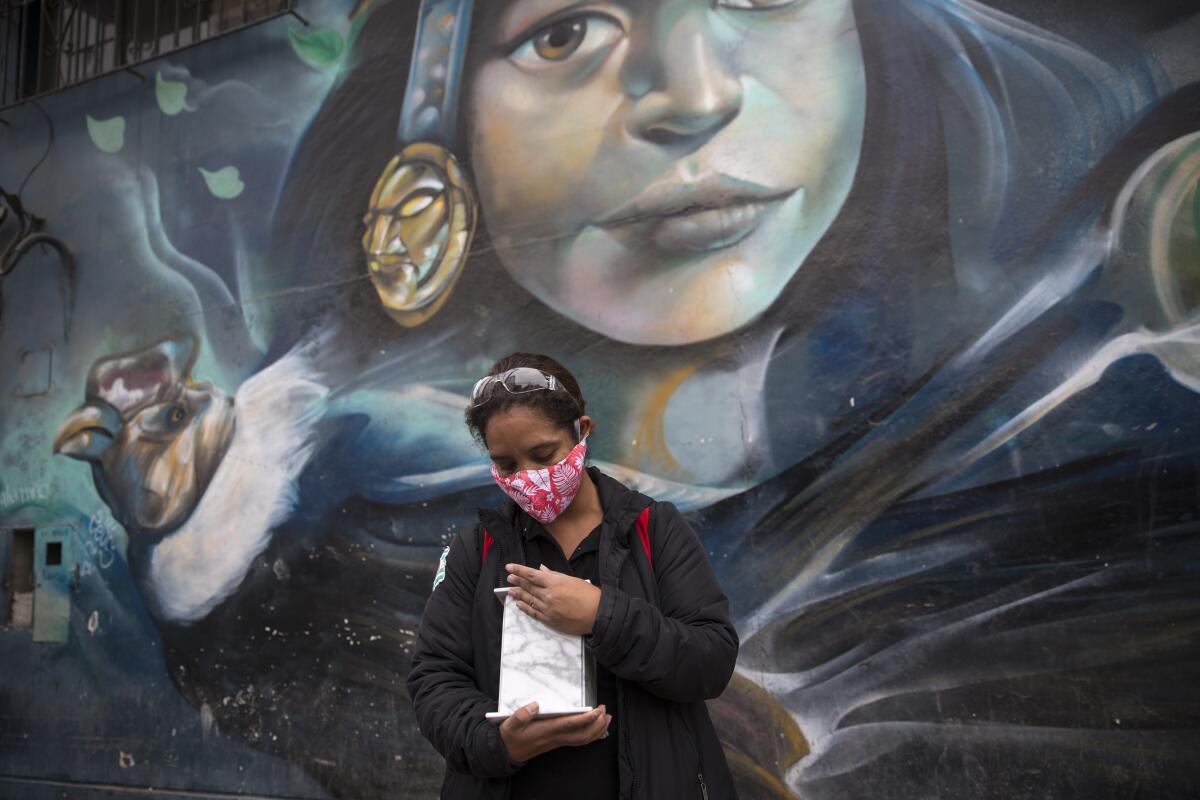 Maritza Lujan, backdropped by a mural painted on a warehouse featuring an Inca princess and condor, caresses the marble urn that contains the cremated remains of her father after a funeral home service delivered them to her at a designated meeting place near her home, in Lima, Peru, Monday, June 22, 2020. Her 67-year-old father, Hugo Lujan, died from symptoms related to COVID-19. (AP Photo/Rodrigo Abd)