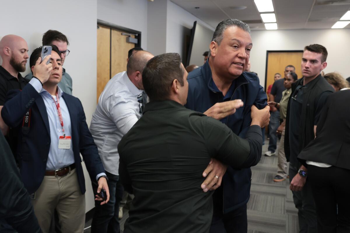 A man in a navy jacket is shoved backward by a shorter man who has his hand on the man's left arm