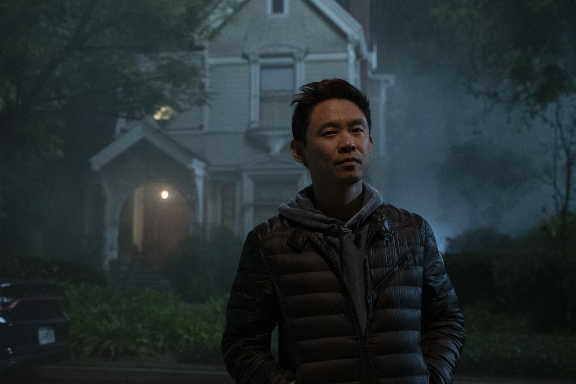 A man in a puffy jacket in front of a spooky-looking house 