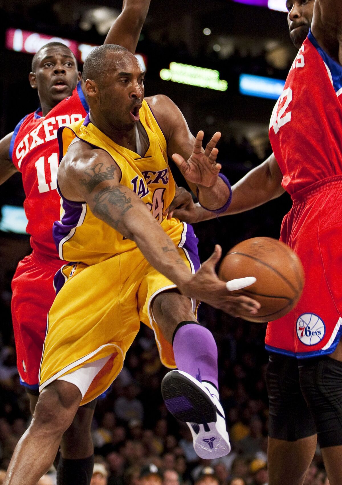 Kobe Bryant passes the ball while being guarded by 76ers guard Jrue Holiday and Elton Brand.