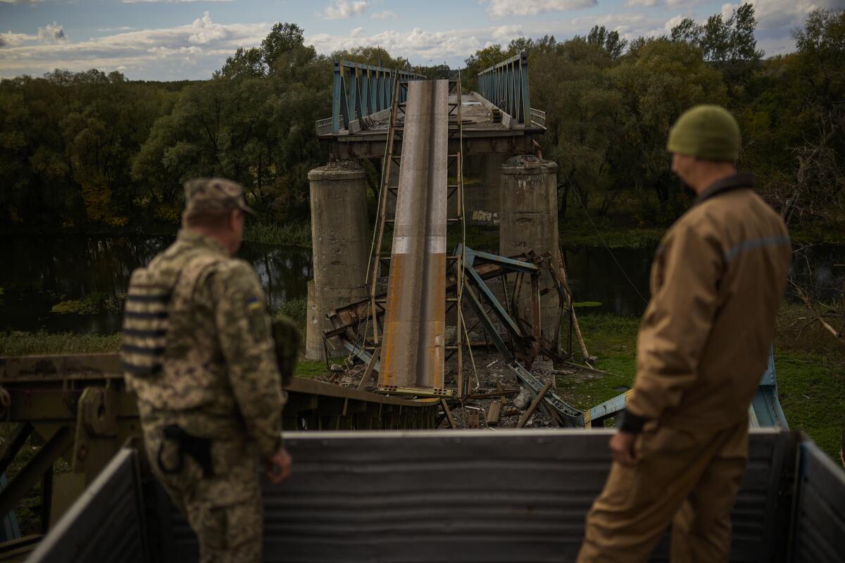 Ukrainian soldiers look at a bridge damaged during fighting.