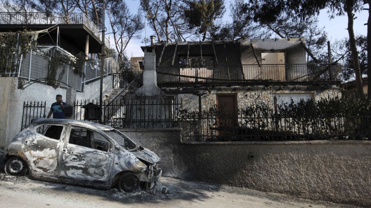 A man speaks on his cellphone next to his burned house and car in Mati, east of Athens, on July 25, 2018.