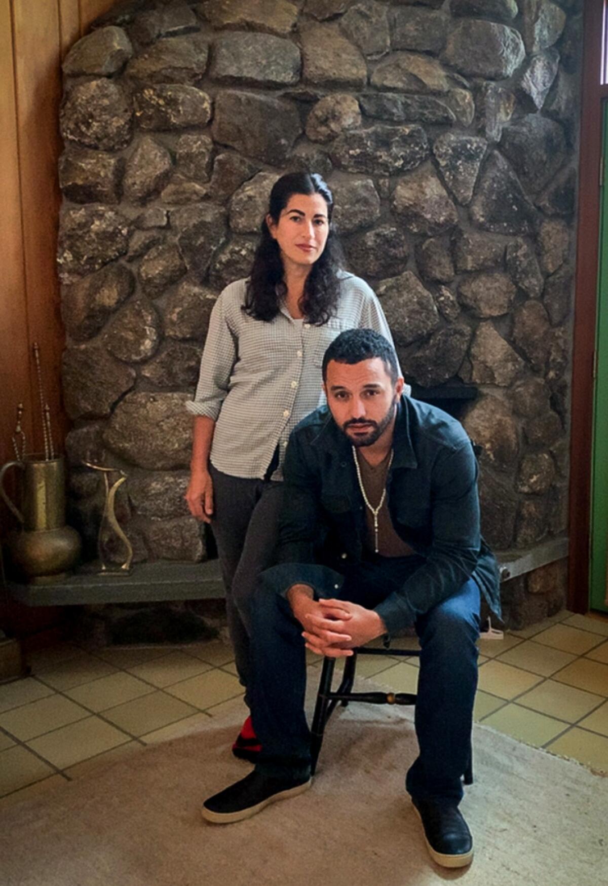 Jehane Noujaim, seated, and Karim Amer in a portrait in front of a fireplace.