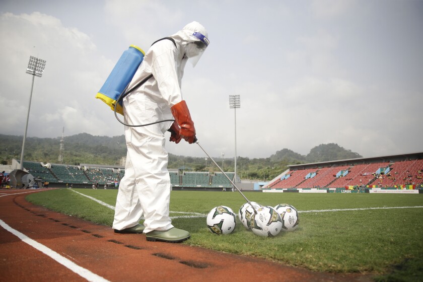 An official wearing protective gear against Covid-19 sprays soccer balls with disinfectant before the African Cup of Nations 2022 group F soccer match between Mauritania and Gambia at the Limbe Omnisport Stadium in Limbe, Cameroon, Wednesday, Jan. 12, 2022. (AP Photo/Sunday Alamba)