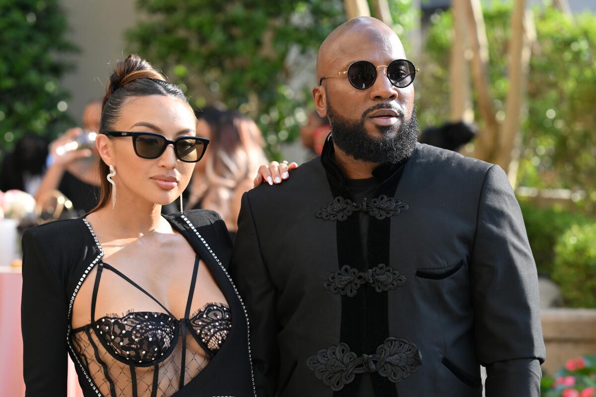 Jeannie Mai in sunglasses and a sheer, strappy black gown holding Jeezy who is wearing sunglasses and a black suit