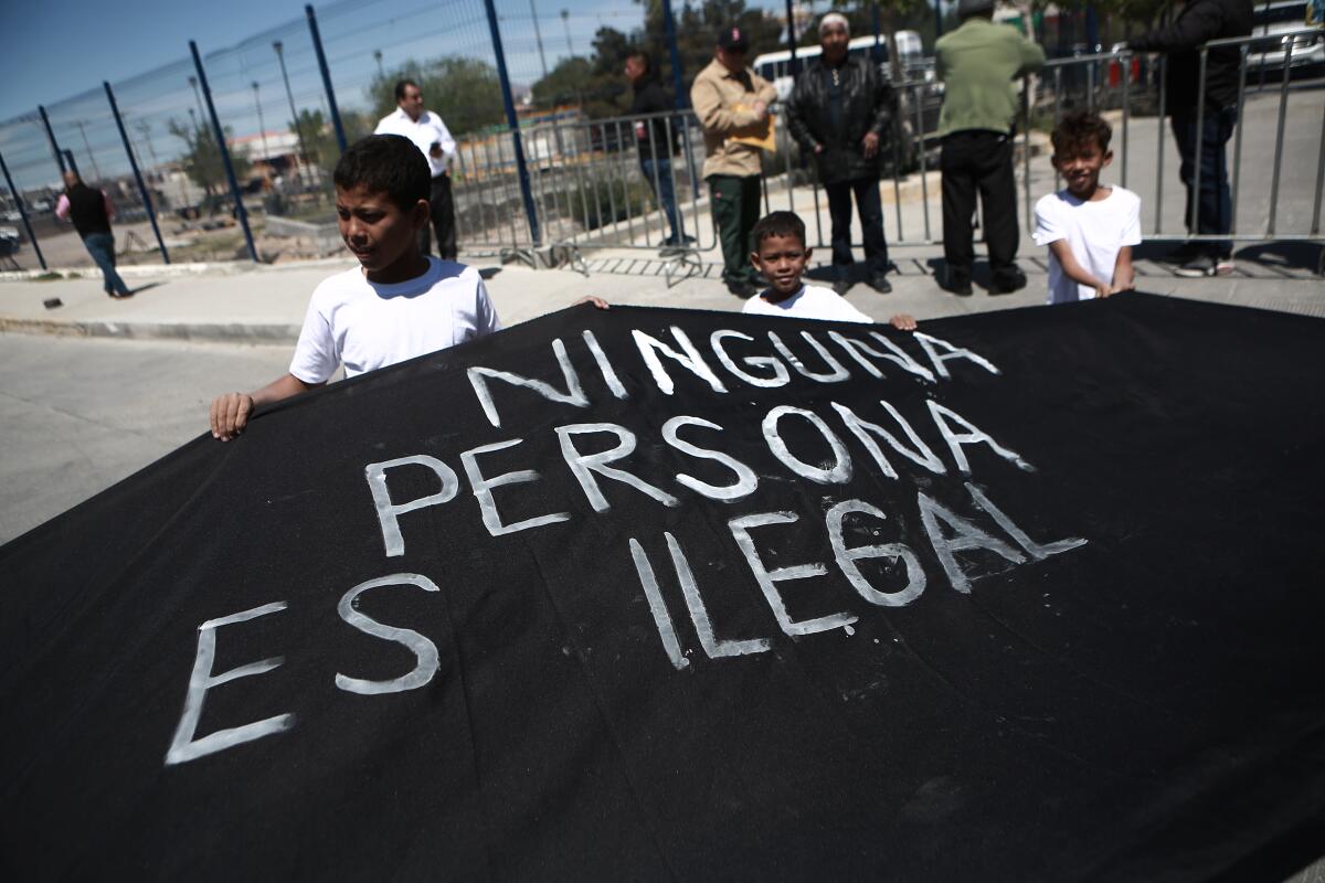 Children hold a black sheet painted with the words in Spanish "no person is illegal" 