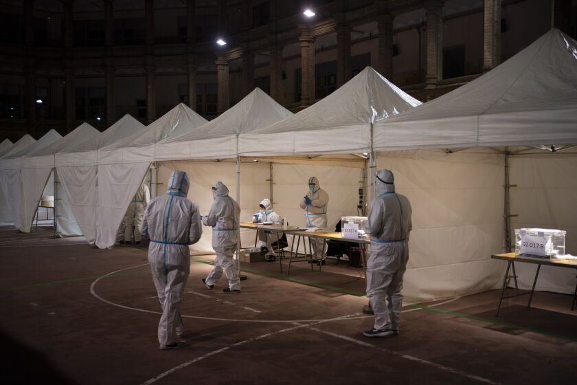 Electoral workers wearing protective suits as a precaution against coronavirus, wait for people to cast their vote at a polling station during the Catalan regional election in Barcelona, Spain, Sunday, Feb. 14, 2021. With Spain still suffering from a post-Christmas spike in coronavirus infections, the vote was held under strict health regulations. Voters were required to wear face masks, use hand disinfectant and remain at least 1.5 meters (5 feet) apart while queuing. (AP Photo/Felipe Dana)
