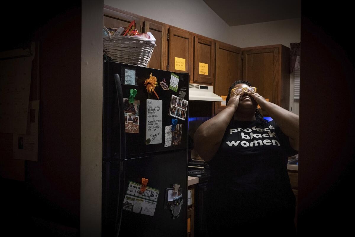 A woman rubs her eyes while standing in her kitchen.