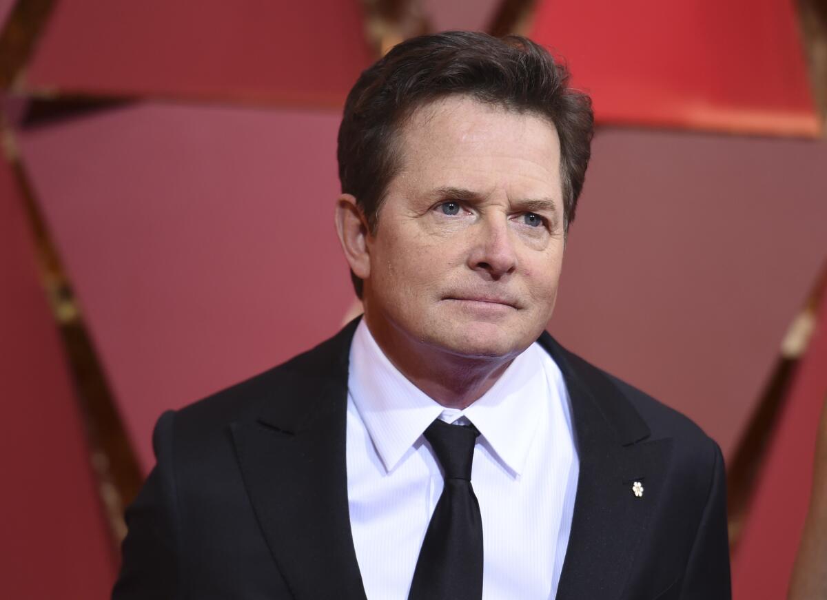 Michael J. Fox wears a white shirt with a dark coat and tie