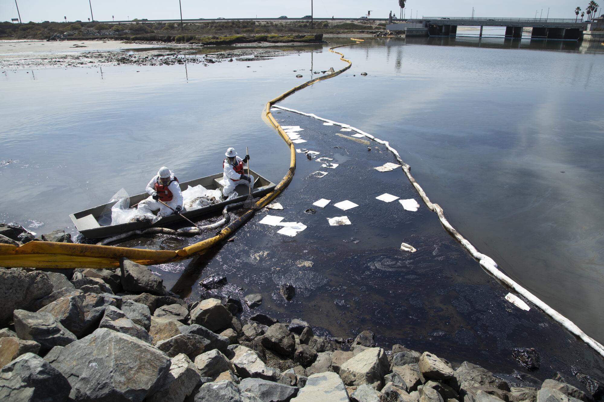 Workers in a boat near booms in a marsh 