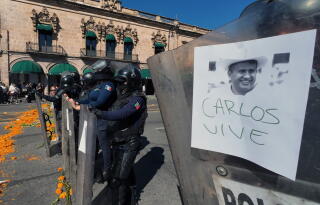 Police officers stand guard as protesters demonstrate against the assassination of Uruapan's mayor