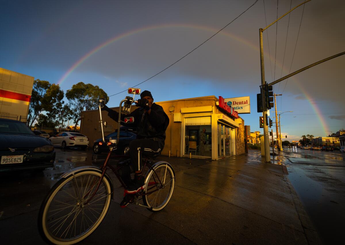 A man rides his bike along Manchester Avenue as a double rainbow forms on Jan. 3.