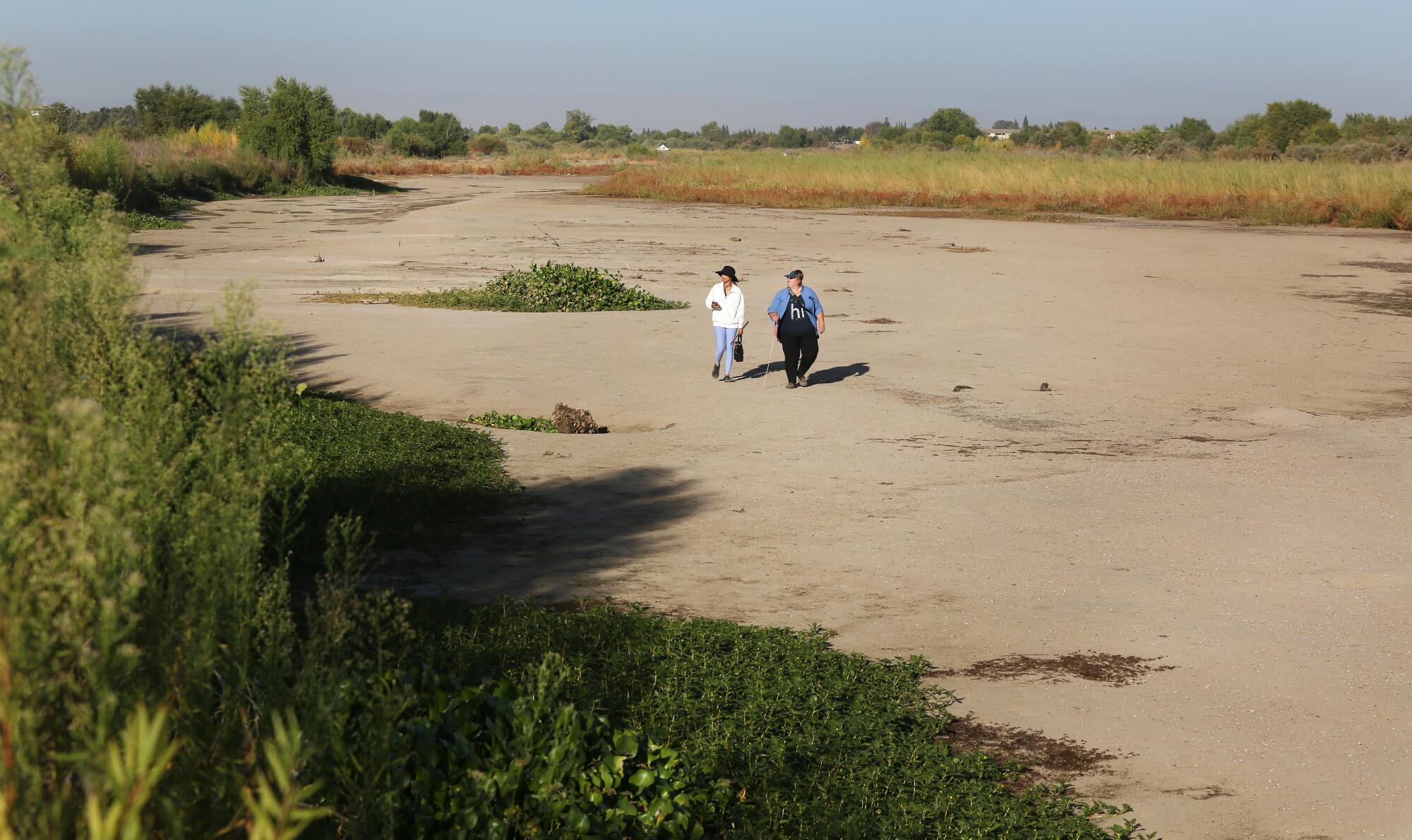 Two women walk in a dry river bed.