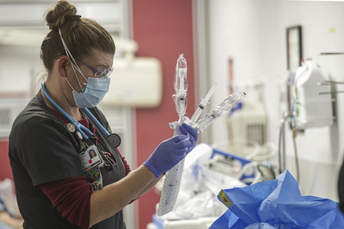 A nurse wearing a face mask holds bagged medical equipment