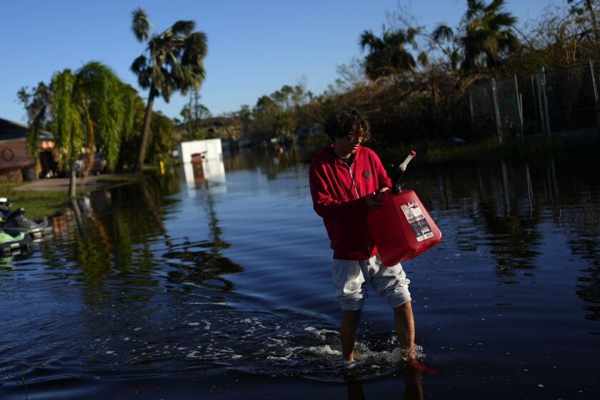 Jose Cruz, 13, carries an empty Jerrycan through receding flood waters outside his house as his family heads out to look for supplies, three days after the passage of Hurricane Ian, in Fort Myers, Fla., Saturday, Oct. 1, 2022. (AP Photo/Rebecca Blackwell)