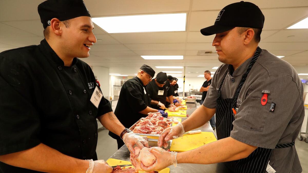 Orlando Ramirez, left, talks with chef instructor Charlie Negrete while breaking down chickens with other students.