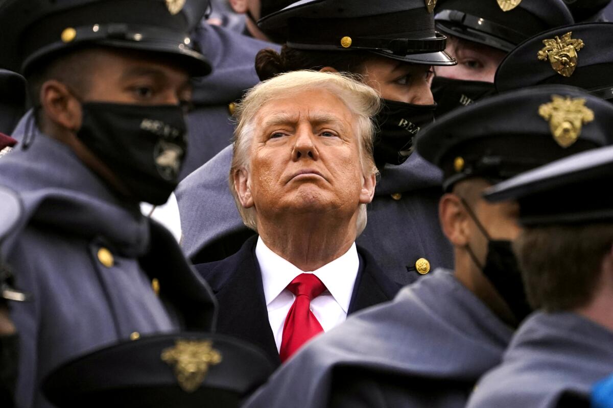 Surrounded by Army cadets in caped coats, hats and masks, an unmasked Trump watches the Army-Navy game from the stands. 