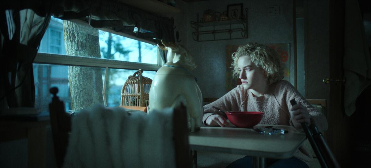 A young woman looks out a window with a bowl of cereal before her