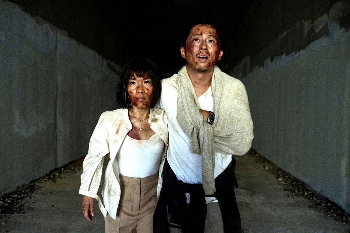 Ali Wong and Steven Yeun, looking roughed up, hold on to each other.