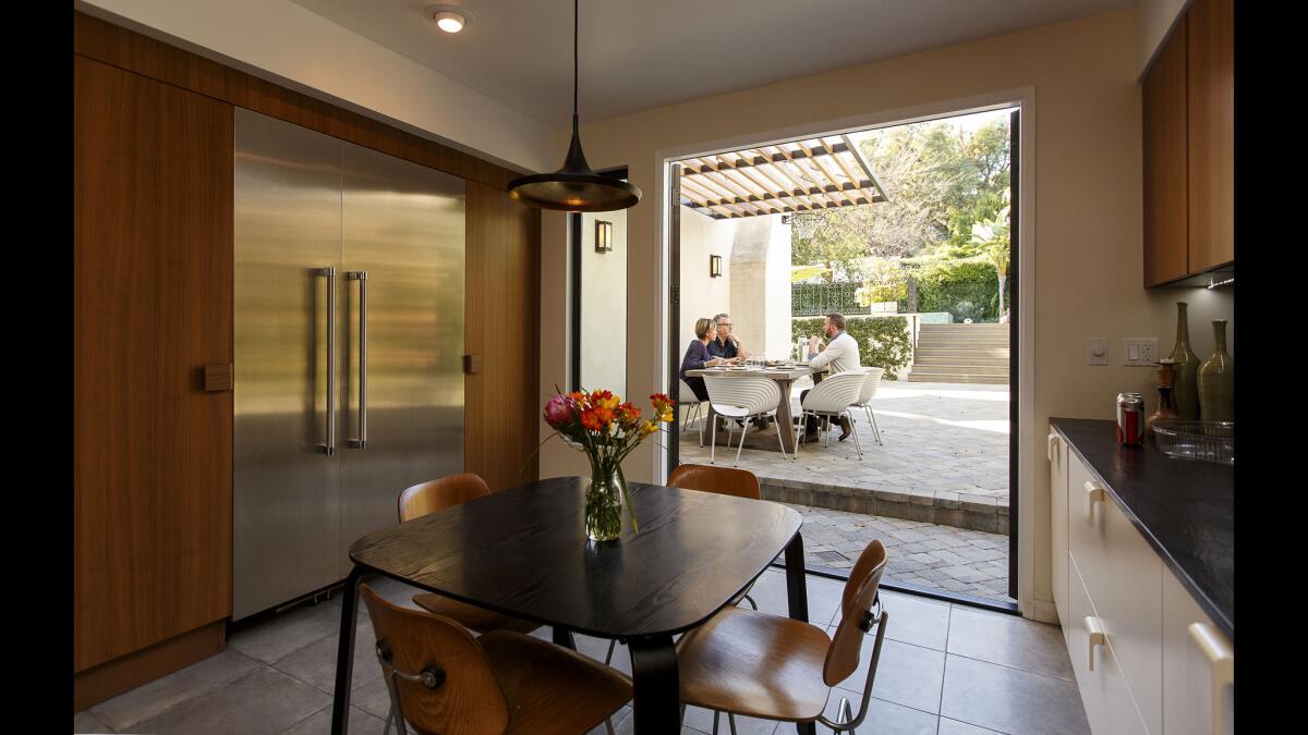 The kitchen, once a dysfunctional jumble of smaller spaces, now has a sleek wall integrating appliances, a porcelain-tiled dining space with vintage Eames chairs and a walkout to an elevated al fresco table.