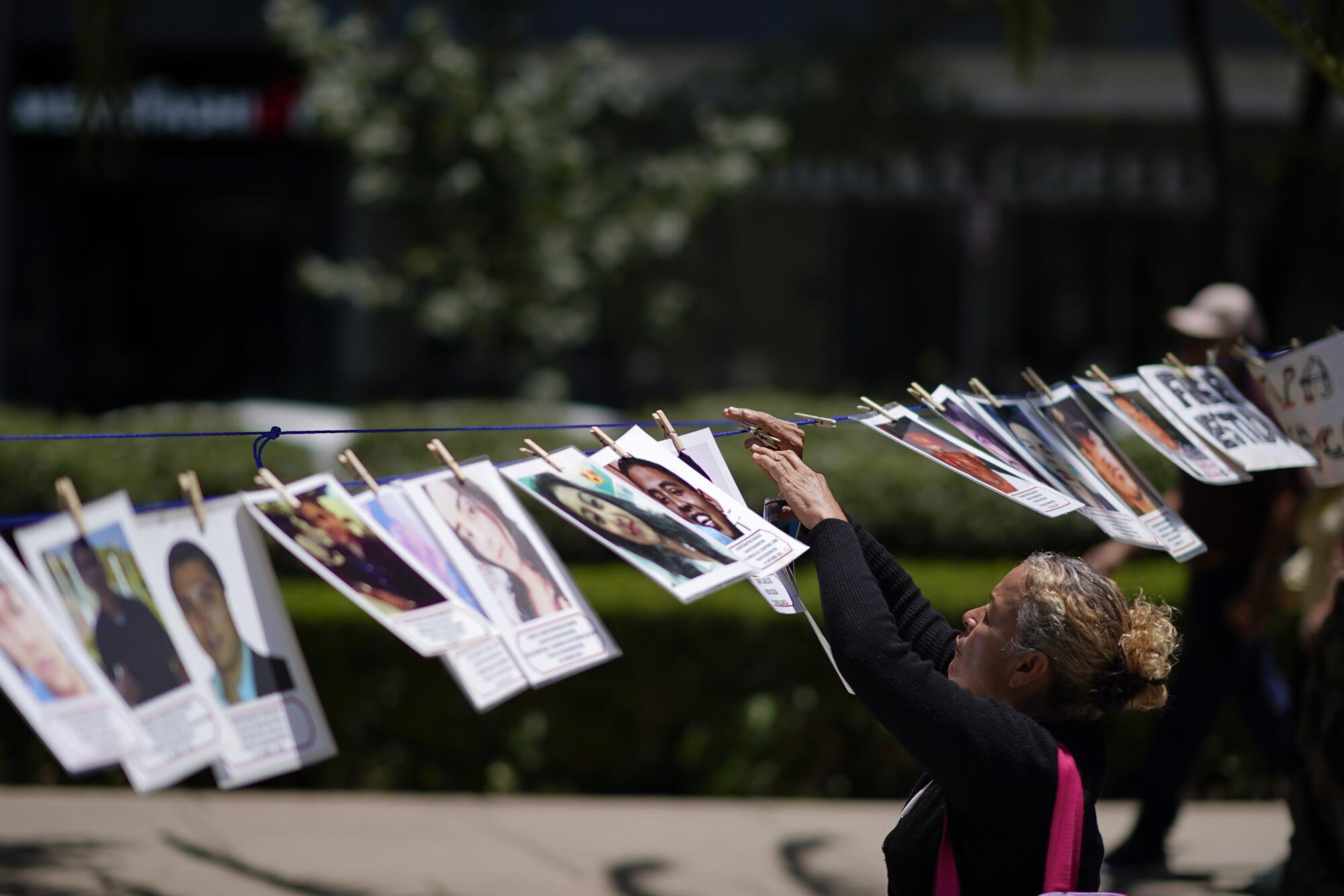 A woman hangs the portrait of a missing person alongside others in a makeshift line along a road.
