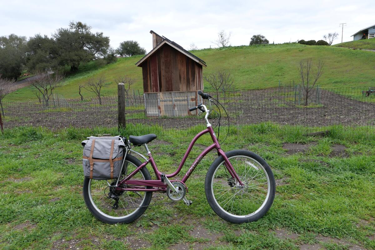 A bicycle on ghe grass in front of a small wooden building with a green hill behind it