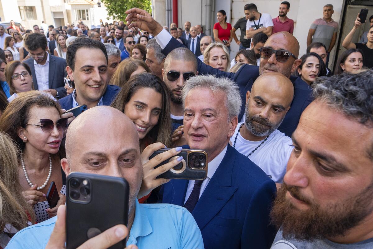 A man in a suit takes selfies surrounded by dozens of people. 