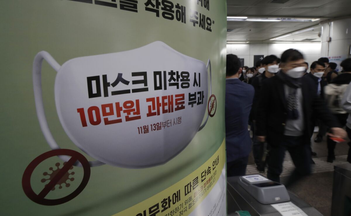 People wearing face masks as a precaution against the coronavirus, walk past near a banner reading: "People who do not wear masks in public will face a 100,000 won ($90) fine", at a subway station in Seoul, South Korea, Friday, Nov. 13, 2020. South Korea has reported its biggest daily jump in COVID-19 cases in 70 days as the government began fining people who fail to wear masks in public. From Friday, officials started to impose fines of up to 100,000 won ($90) for people who fail to properly wear masks in public transport and a wide range of venues, including hospitals, nursing homes, pharmacies, nightclubs, karaoke bars, religious and sports facilities and at gatherings of more than 500 people. (AP Photo/Lee Jin-man)