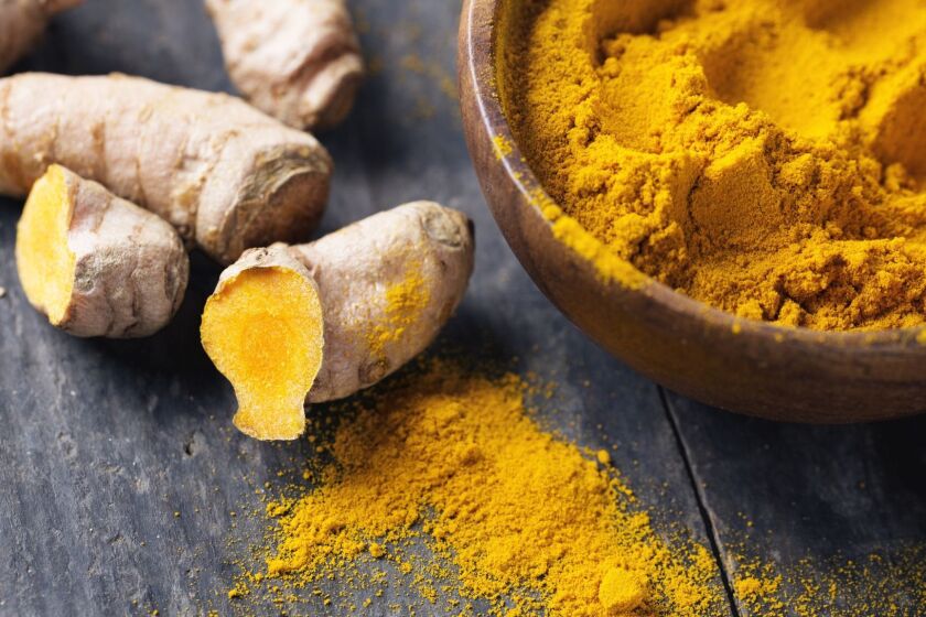 Freh turmeric roots and turmeric powder in a wooden bowl on rustic wood