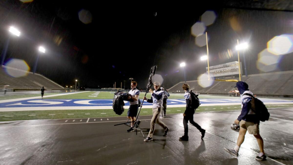 Corona del Mar High football players walk with video equipment after the Sunset League game against Los Alamitos was called due to lightning on Friday.