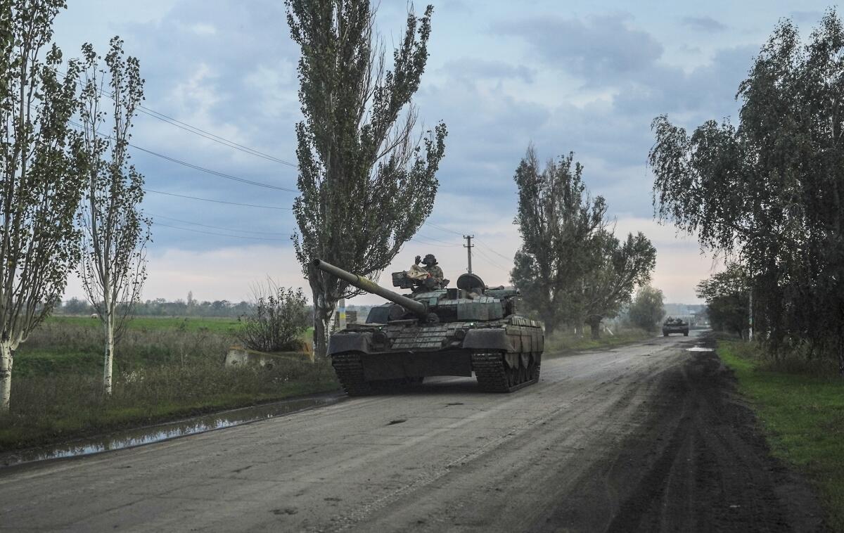 A Ukrainian tank heads down a road next to an open field.
