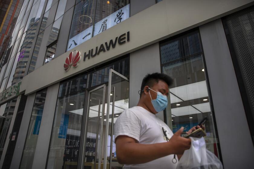 FILE - In this Wednesday, July 1, 2020 file photo, a man wearing a face mask to protect against the new coronavirus looks at his smartphone as he walks past a Huawei store in Beijing. The British government is reportedly poised to backtrack on plans to give Chinese telecommunications giant Huawei a limited role in the U.K.‘s new high-speed mobile phone network, a decision with broad implications for relations between the two countries. Britain’s decision to re-examine the question, the results of which will be announced Tuesday, July 14 came after the U.S. threatened to sever an intelligence-sharing arrangement because of concerns Huawei equipment could allow the Beijing government to infiltrate U.K. networks. (AP Photo/Mark Schiefelbein, file)