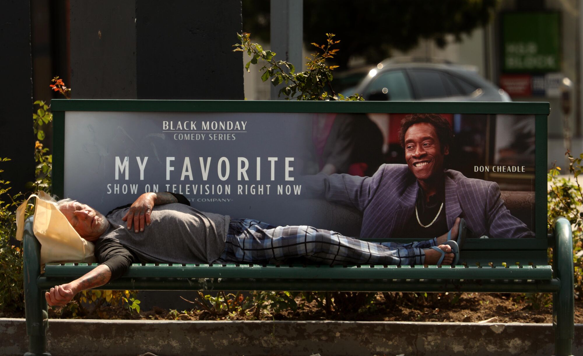 A homeless man by the name of Loren, sleeps on a bench under the watchful eye of actor Don Cheadle in East Hollywood