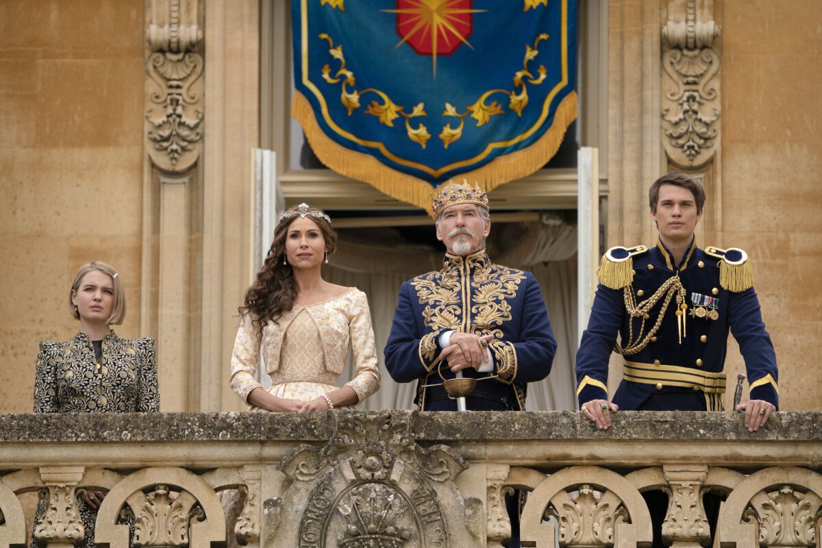 A royal family of four stands on a balcony