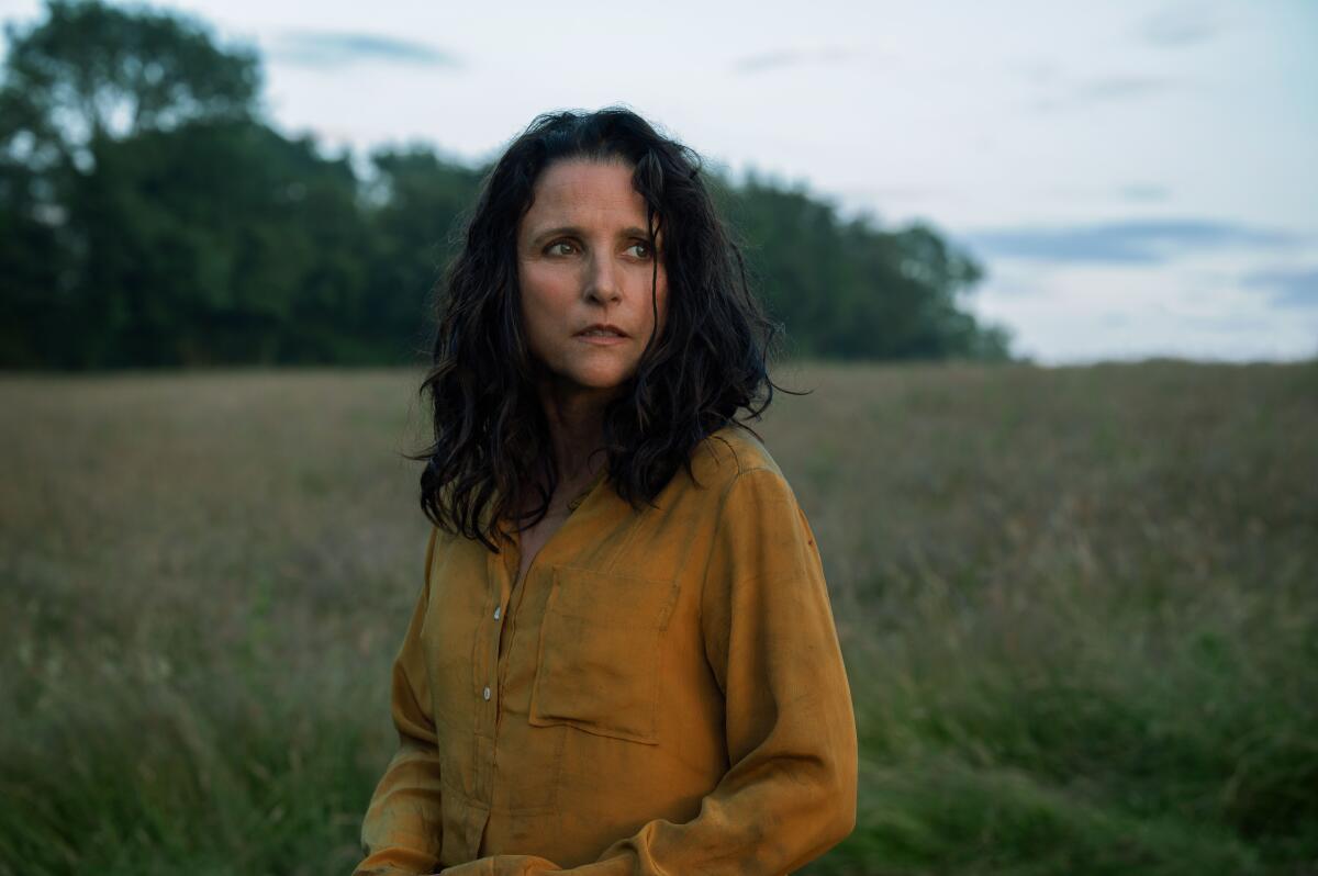 Julia Louis-Dreyfus stands in a field, a thoughtful expression on her face.