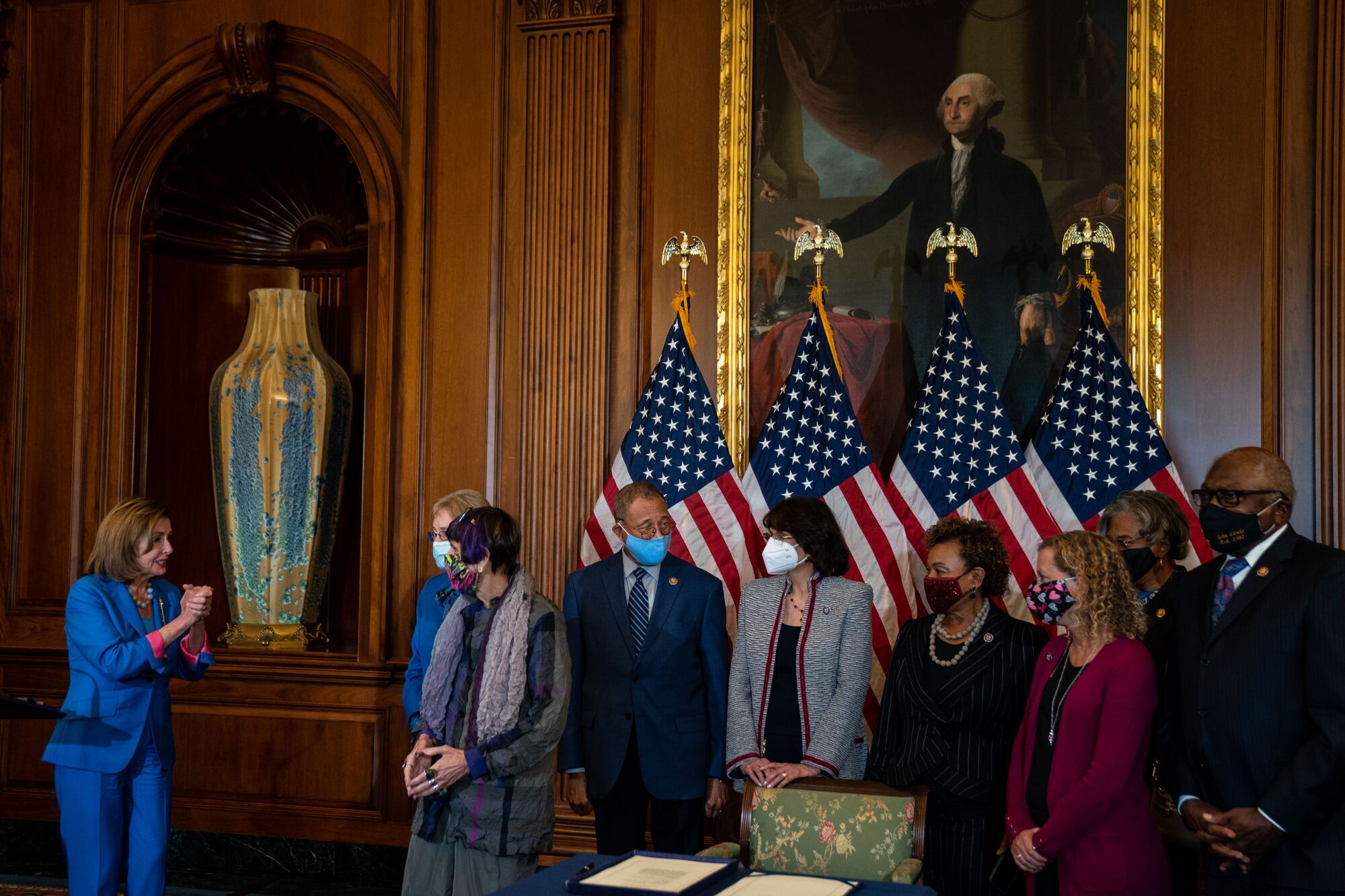Nancy Pelosi, left, talks with eight others standing before four U.S. flags