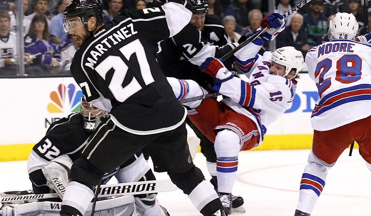 Kings defenseman Alec Martinez and goalie Jonathan Quick look for the puck behind the net while teammate Matt Greene knocks Rangers forward Derek Dorsett out of the crease during the second period of Game 1 of the Stanley Cup Final.