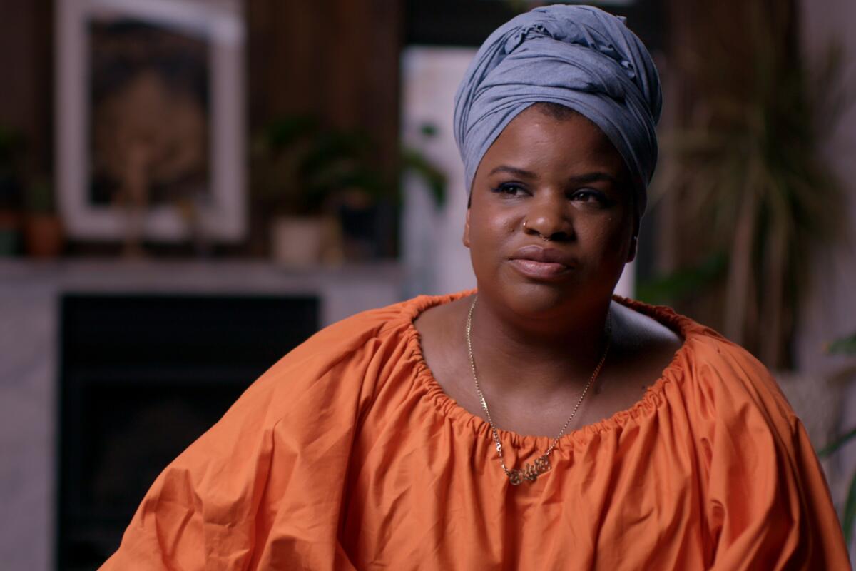 A woman in an orange blouse and blue fabric headwrap.
