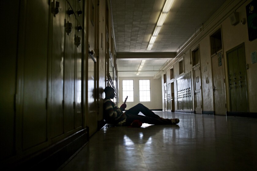 A student sits on the floor leaning against lockers in a school hallway