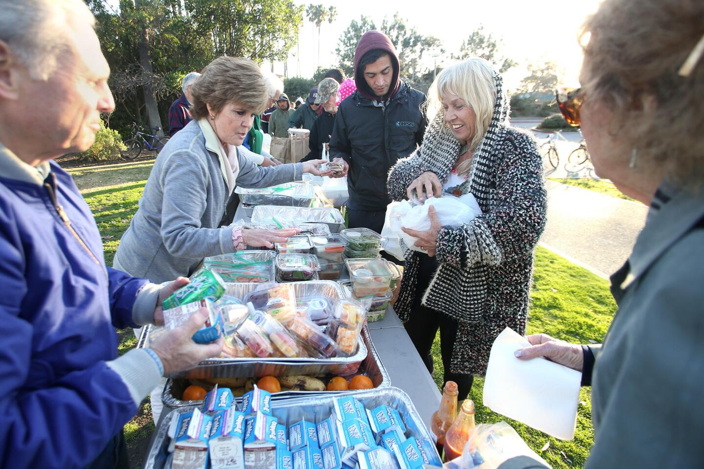 Volunteers, from left, Glenn Wood, Jeannie Karcher and Moira Obermeyer share a laugh with a guest who stands in line at the Welcome Inn, an interfaith meal service at Doheny State Beach on recent evening.