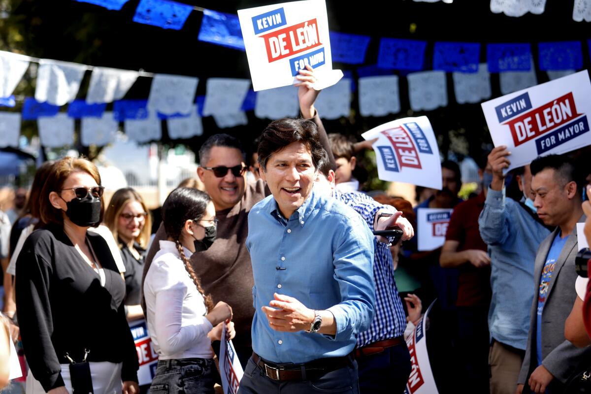 A man is surrounded by supporters holding signs reading "Kevin de Leon for mayor"