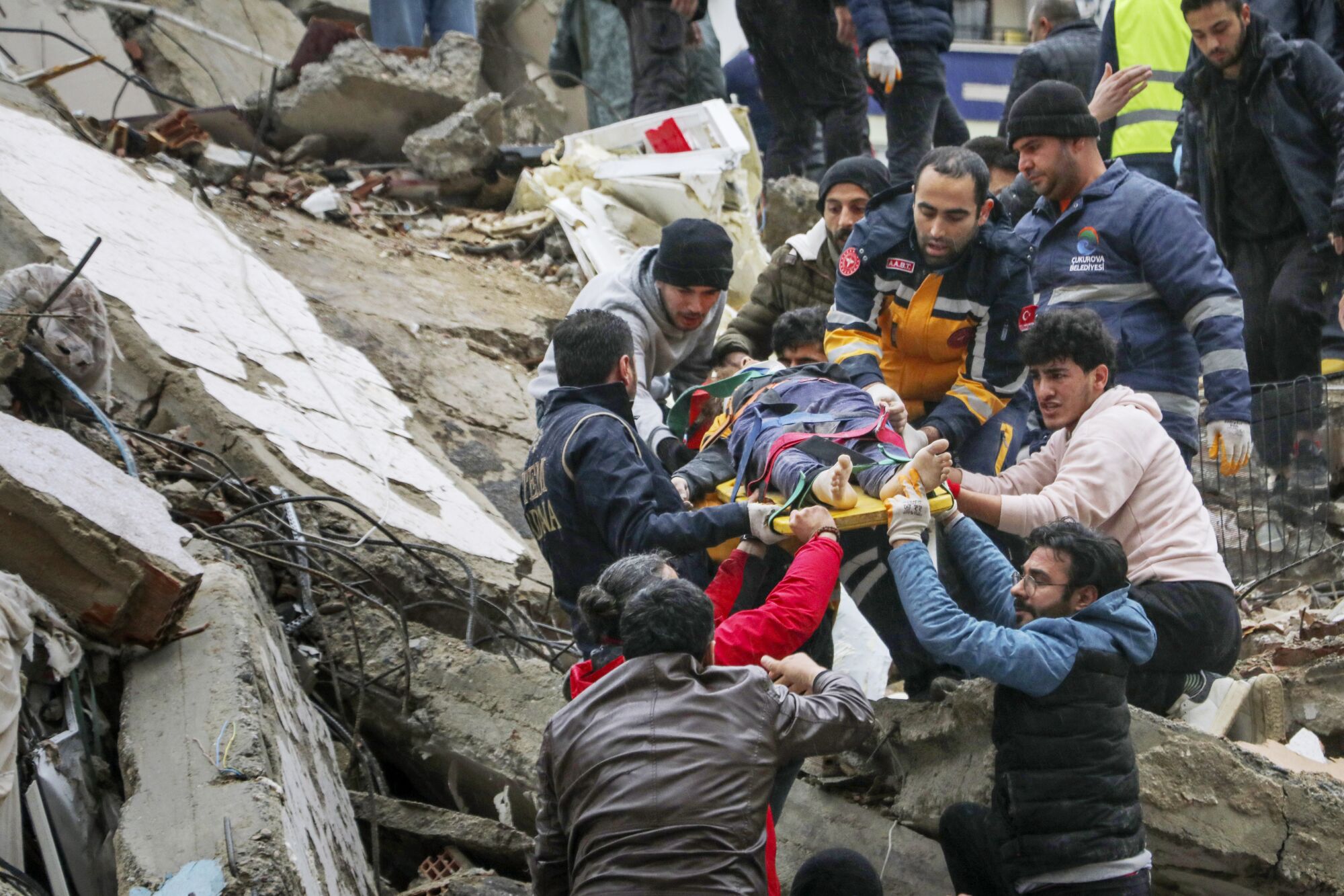 People and emergency teams rescue a person on a stretcher from a collapsed building.