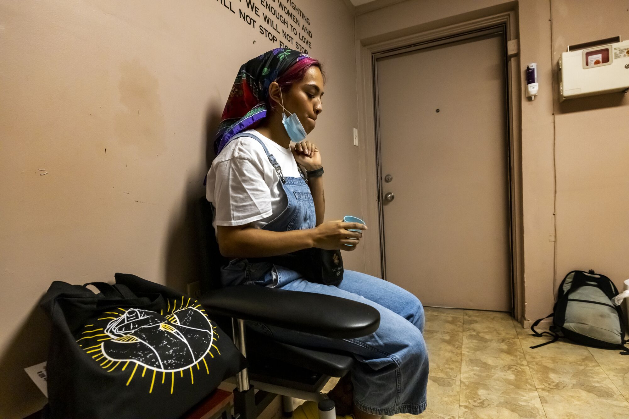 A woman sits in a chair with a blue cup in her hand.