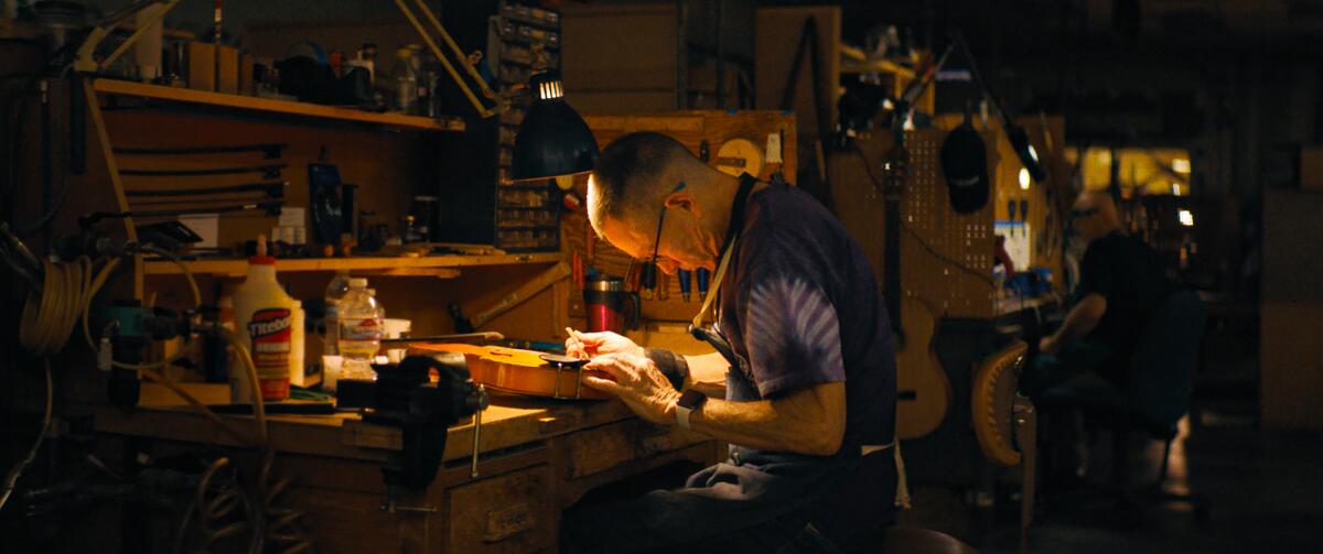 A man leans close to work on repairing a string instrument in "The last repair shop."