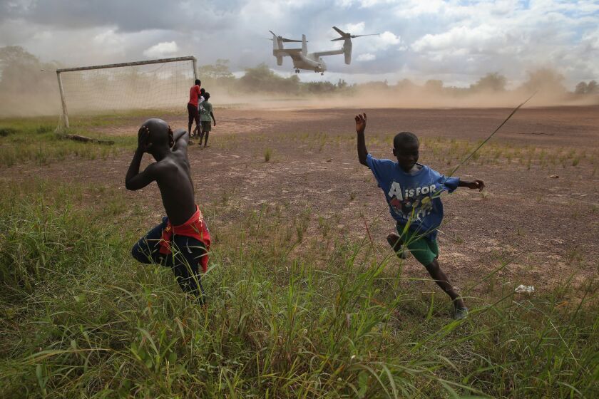 Boys run from the blowing dust as a U.S. aircraft departs the site of an Ebola treatment center under construction in Tubmanburg, Liberia, on Oct. 15. The center was the first of 17 built by Liberian forces under U.S. supervision.
