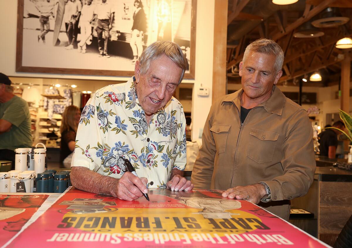 Surfing pioneer Dick Metz, left, and director Richard Yelland autograph posters on Nov. 10.