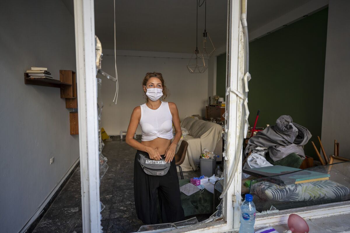 Sandrine Zeinoun, 34, poses for a photograph inside her destroyed apartment after Tuesday's explosion in the seaport of Beirut, Lebanon, Thursday, Aug. 6, 2020. The gigantic explosion in Beirut on Tuesday tore through homes, blowing off doors and windows, toppling cupboards, and sent flying books, shelves, lamps and everything else. Within a few tragic seconds, more than a quarter of a million people of the Lebanese capital's residents were left with homes unfit to live in. Around 6,200 buildings are estimated to be damaged. (AP Photo/Hassan Ammar)