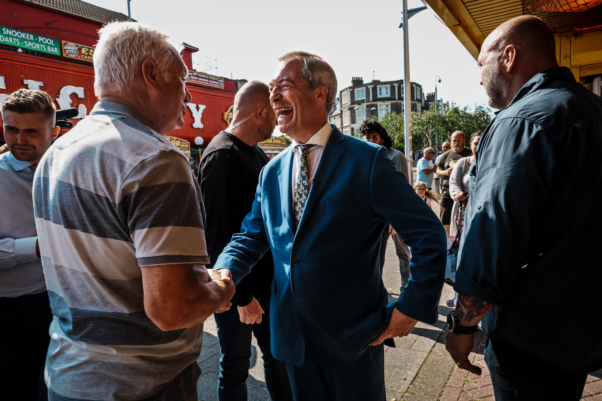 Nigel Farage sorri largamente e aperta a mão de um homem. 