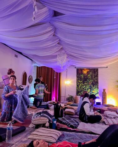 People lie or sit on mats under a fabric-swagged ceiling in a white-walled room